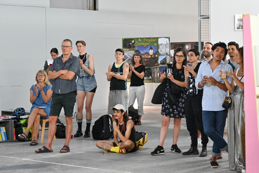 KI generiert: Das Bild zeigt eine Gruppe von Menschen, die scheinbar an einer Veranstaltung oder Präsentation teilnehmen. Sie stehen oder sitzen, schauen in dieselbe Richtung und wirken aufmerksam und interessiert.