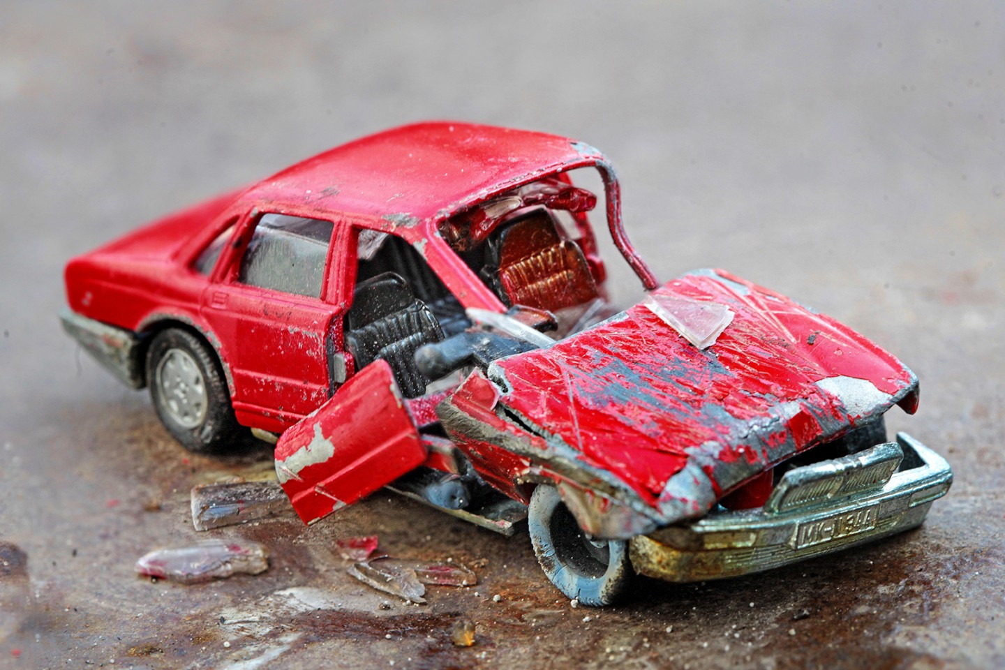 KI generiert: Das Bild zeigt ein stark beschädigtes rotes Spielzeugauto mit eingedrückter Frontpartie und offenen Türen. Es wirkt wie ein Unfallauto, das auf einer Oberfläche steht.