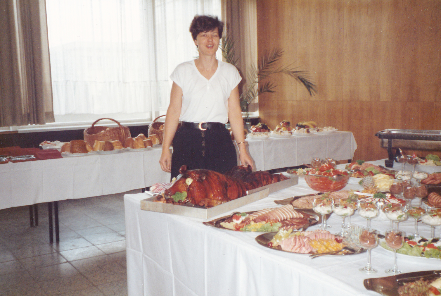 AI generated: A woman stands next to a richly laid buffet with a variety of dishes, including meat dishes and salads. The focus of the image is on the opulent presentation of the food.