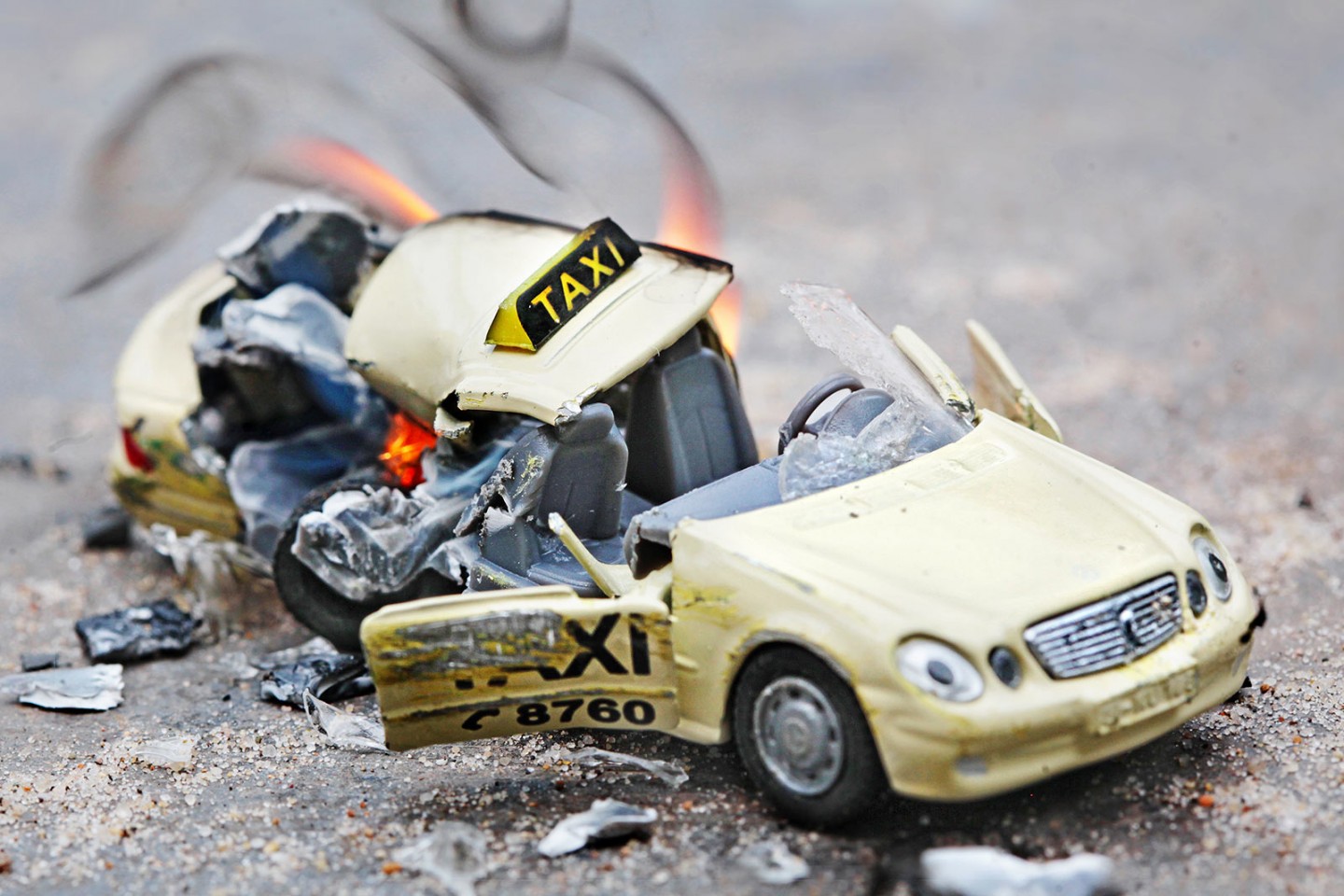 KI generiert: Das Bild zeigt ein Modellauto eines Taxis, das stark verformt und beschädigt ist und teilweise in Flammen steht. Es vermittelt den Eindruck eines schweren Unfalls oder einer Explosion.