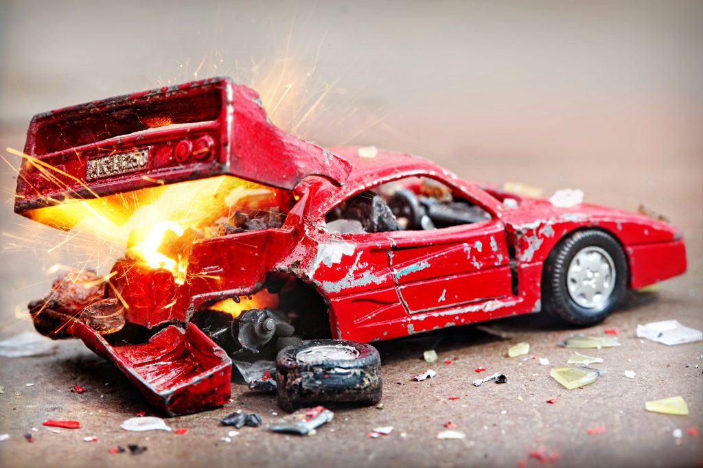 KI generiert: Das Bild zeigt ein stark beschädigtes rotes Spielzeugauto mit funkelnden Funken und Trümmern, die um das Fahrzeug verstreut sind. Es scheint eine Explosion oder ein schwerer Unfall dargestellt zu sein.