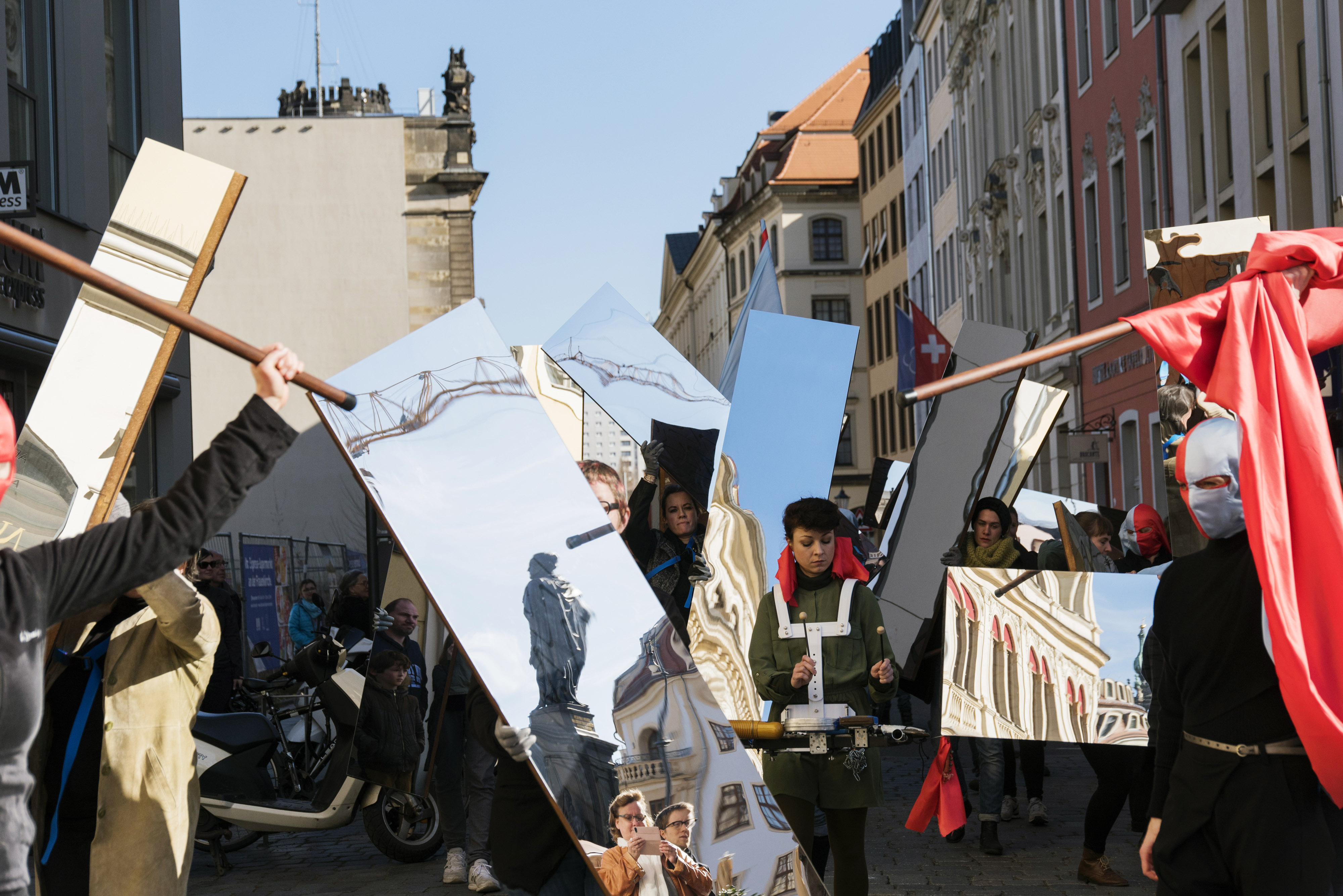 KI generiert: Das Bild zeigt eine Gruppe von Menschen, die auf einer Straße Spiegel tragen, wobei manche Teilnehmer maskiert sind. Die Szenerie suggeriert eine Art Demonstration oder Kunstperformance in einem städtischen Umfeld.