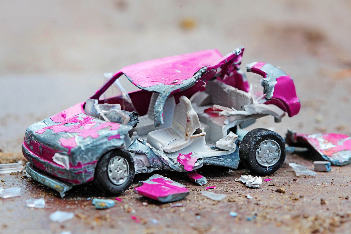 KI generiert: Das Bild zeigt ein stark beschädigtes und verbogenes Spielzeugauto mit einer zerrissenen und farblich abblätternden Karosserie. Das Auto liegt auf einer schmutzigen Oberfläche und ist teilweise auseinandergebrochen, umgeben von kleinen Trümmerteilen.